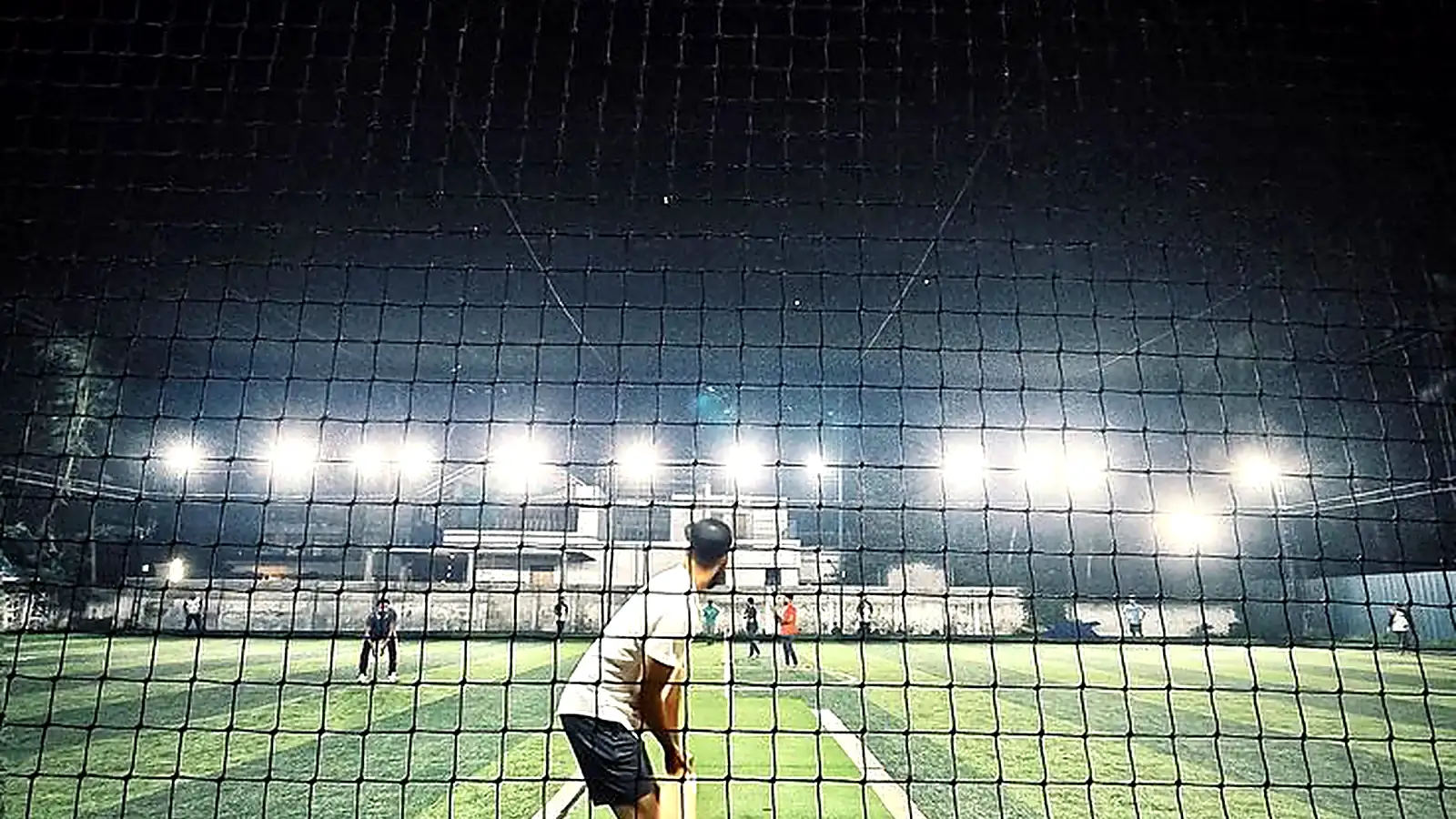 A batter waiting at the crease under floodlights on a box cricket turf