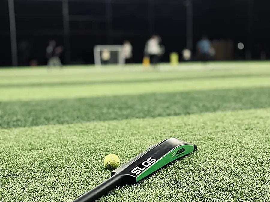 A bat and tennis ball resting on the turf under floodlights